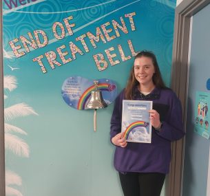 Ellie smiling next to the end of treatment bell