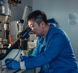Male researcher in blue labcoat looking at microscope
