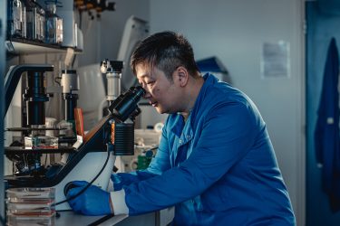 Male researcher in blue labcoat looking at microscope