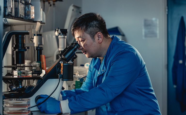 Male researcher in blue labcoat looking at microscope